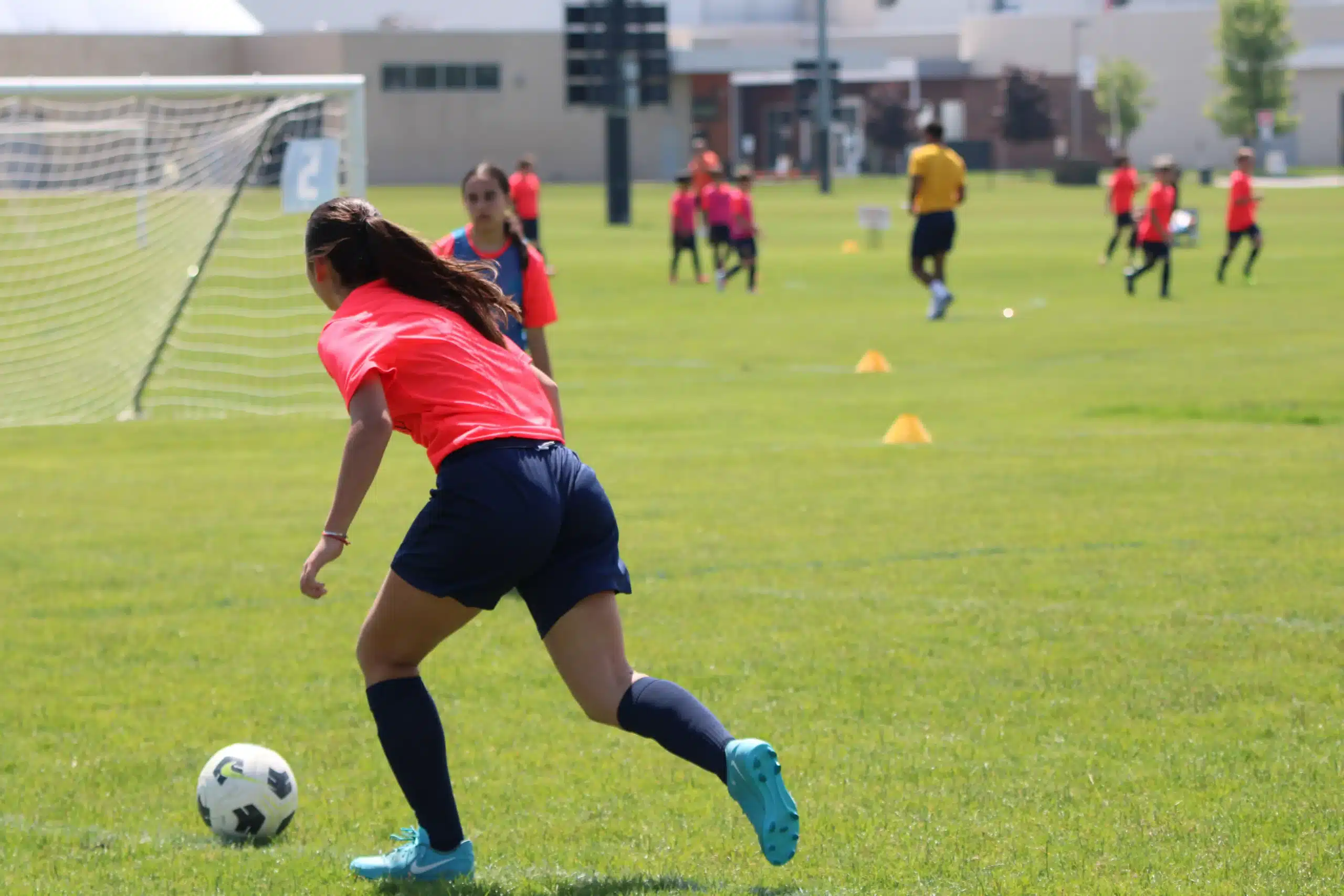 A young player wears best soccer cleats for kids while dribbling a soccer ball on a grass field during a sunny outdoor training session.